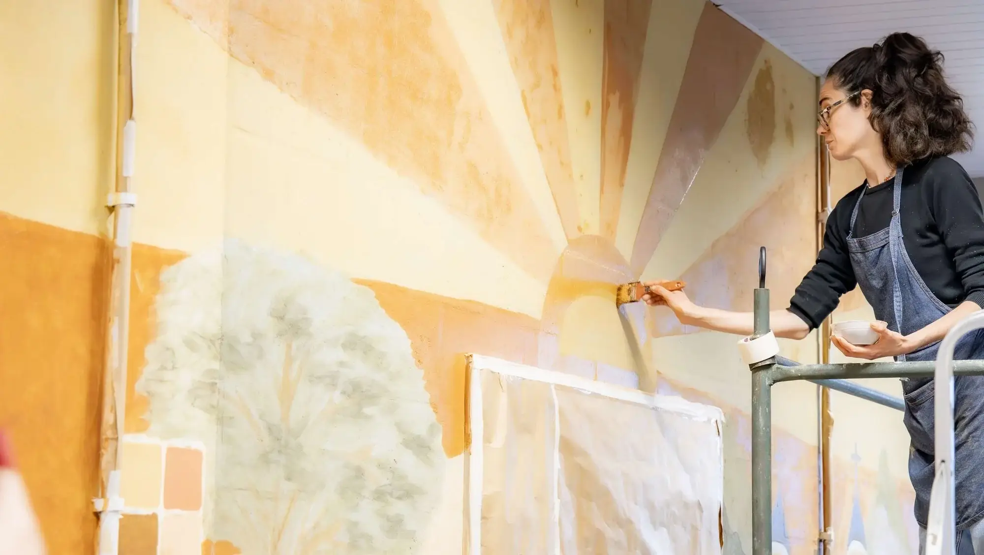 Marcela da Terra pintando um mural em tintas de terra sobre andaime, no I Encontro Nacional do SESC Comunidade em Biguaçu