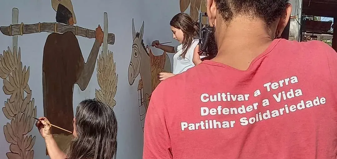 Participantes pintando figuras do mural coletivo na parede da escola