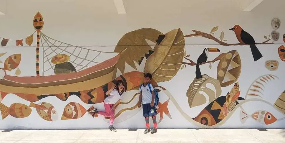 Mural em tintas de terra no Colégio CEMBRA em Paraty, com canoa, peixes, tucano e folhas em tons de ocre e terracota