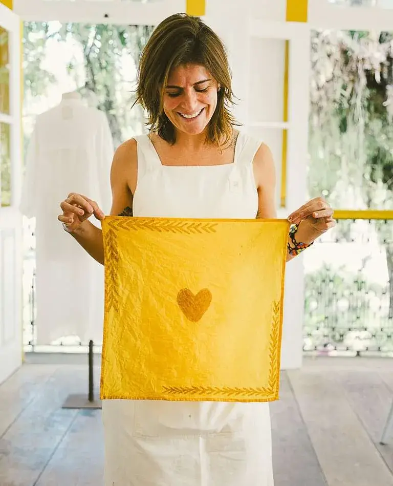Participante segurando um lenço tingido de amarelo com estampa botânica de folhas e coração